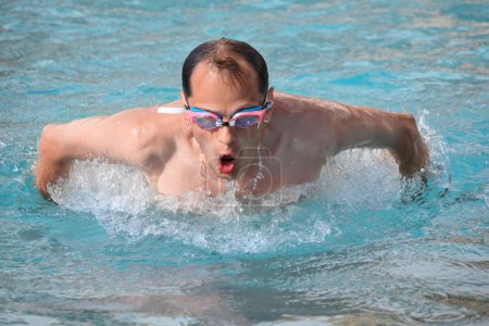 Young man in watersport goggles swimming in pool, jumped out of