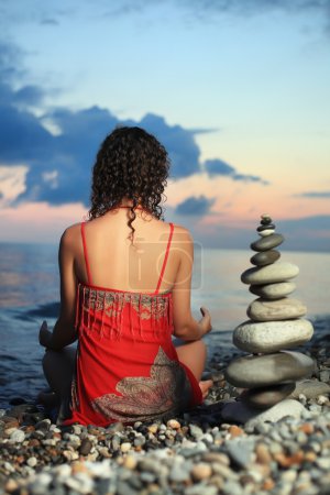 Beautiful woman in red sundress meditating near to pyramid from