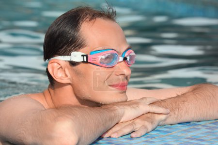 Young man in watersport goggles swimming in pool, near ledge