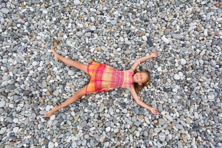 Little girl lying on stones on stone seacoast