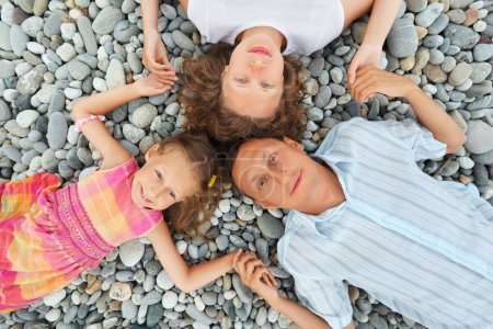 Happy family with little girl lying on stony beach, having joine