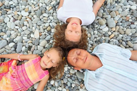 Happy family with little girl lying on stony beach, closed eyes,