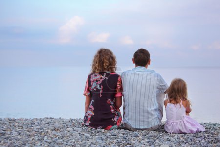 Happy family with little girl sitting on stony beach, sitting by