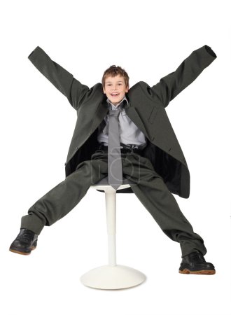 Little boy in big grey man's suit sitting on chair and smiling i