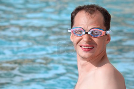 Smiling young man in watersport goggles swimming in pool