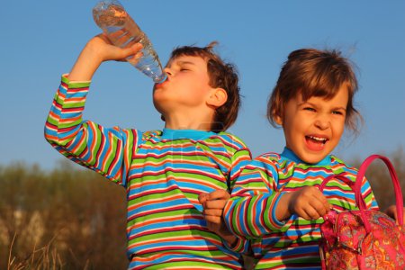 Two children in striped T-shirts, boy drinks from bottle, gir