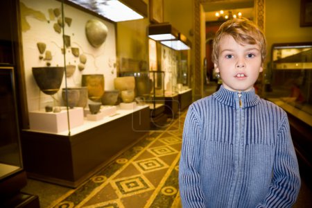 Boy at excursion in historical museum near exhibits of ancient r