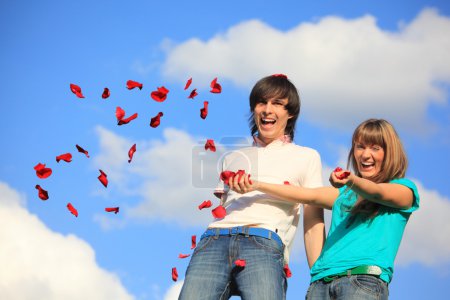 Young pair scatters petals of roses against sky