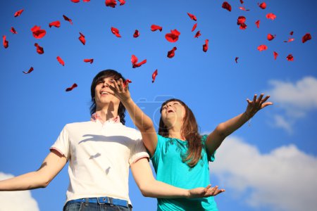 Young pair scatters petals of roses against sky