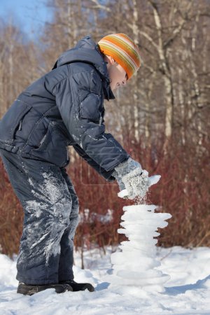 Boy creates pyramid from ice in sunny day in winter in wood, Un