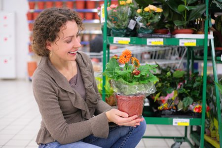 Young woman holds pot with flower in shop