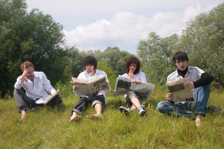 Four friends read newspapers on grass