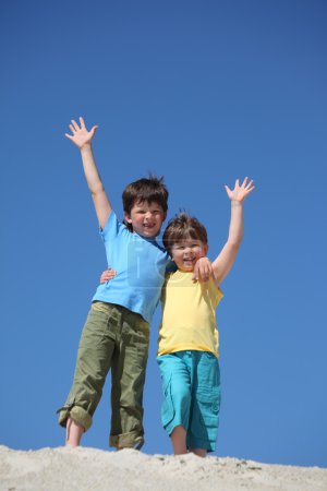 Two boys stand on sand and lifted hands in greeting