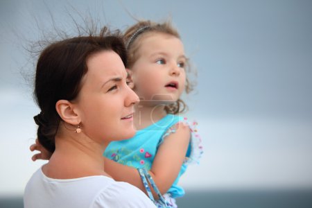 Beautiful woman protects little girl from wind on seacoast