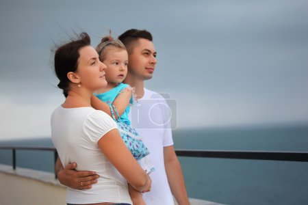 Young man and beautiful woman protects little girl from wind on