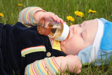 Child drinks from a bottle laying in grass