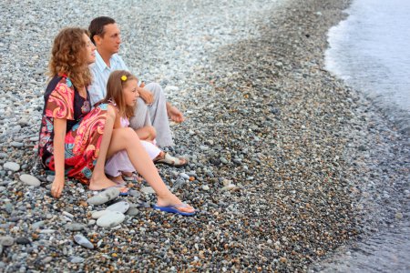 Happy family with little girl sitting on stony beach, Looking af