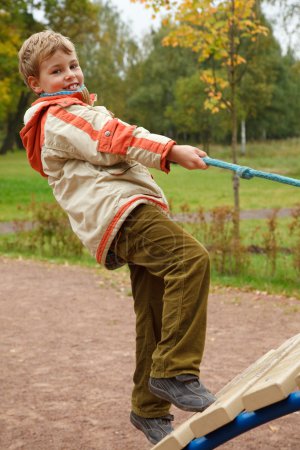 Boy in jacket is on playground in autumn park