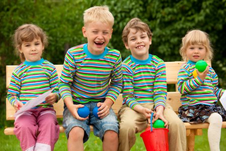 Four children in identical clothes laugh sitting on a bench.