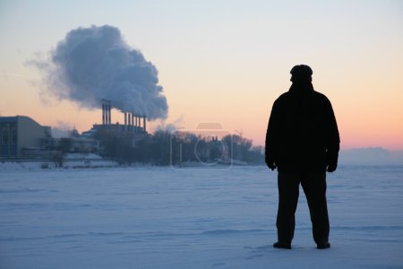Man stand on the frozen river near smoking pipes
