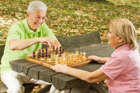 Happy senior couple playing chess on a park bench