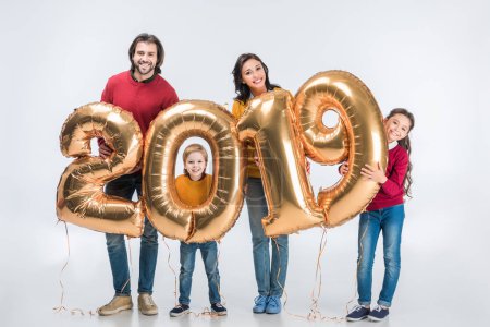 Happy family holding golden 2019 sign balloons for new year and looking at camera isolated on white 