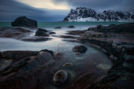 Uttakleiv rocky coast with mountains in background at cloudy sunset, Norway