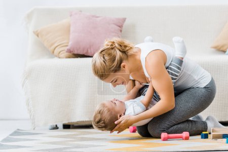 smiling woman playing with adorable toddler boy on carpet in living room