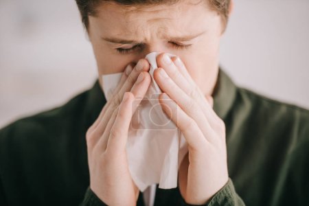 close up of man sneezing in tissue at home 