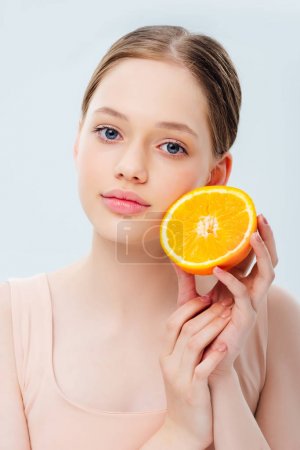 beautiful teenage girl holding ripe orange half isolated on grey