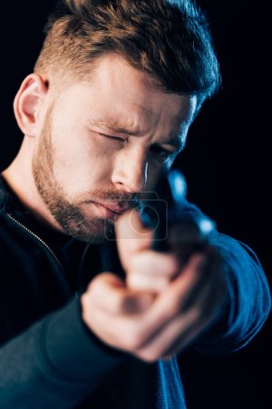 bearded criminal aiming gun at camera isolated on black