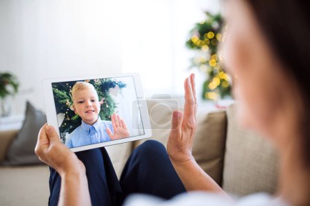 A grandmother with tablet making videocall with small grandson at Christmas time.