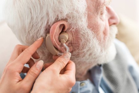 Cropped view of woman helping grey haired man, wearing hearing aid