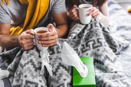 cropped view of sick girlfriend and boyfriend holding cups with tea 