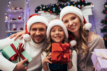 happy kid in santa hat holding christmas present near parents