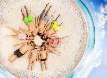 Aerial view of big group of boys and girls, happy friends, laying in a circle on sandy beach in summer