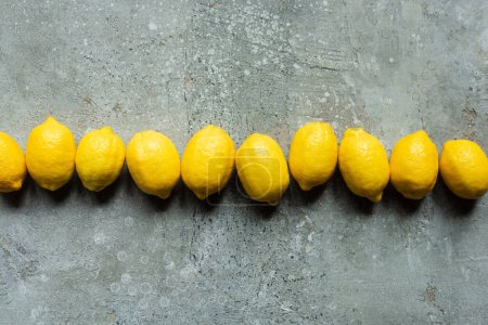 top view of ripe yellow lemons in row on concrete textured surface