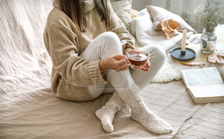 Cozy autumn or winter at home, a woman in a knitted sweater with a Cup of tea and a book .