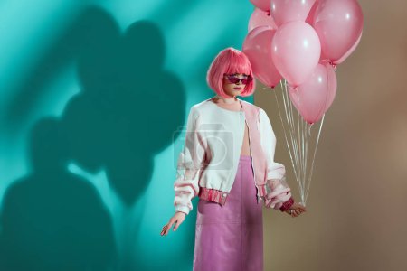 stylish pretty girl in bright wig holding pink balloons and looking away