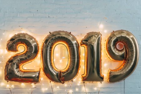 2019 golden balloons with light garland on white wall for new year