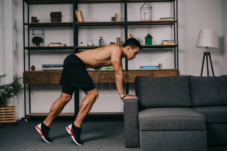 muscular mixed race man exercising near sofa in living room 
