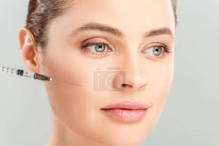 close up of syringe near face of attractive woman isolated on grey 