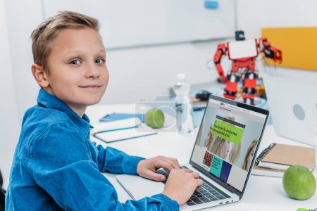 smiling boy using laptop with science website on screen and taking psychological test