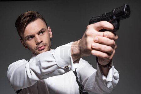 handsome secret agent aiming with handgun isolated on grey