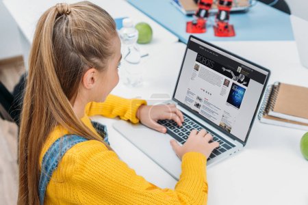 schoolgirl using laptop with science website on screen and reading article about robots