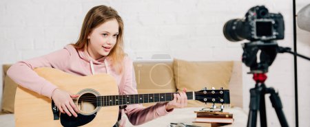 Panoramic shot of teenage blogger playing acoustic guitar in front of video camera