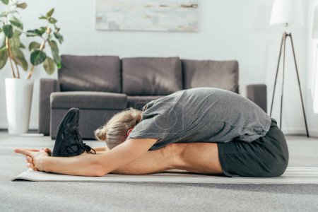 side view of sporty adult man exercising and stretching on yoga mat at home