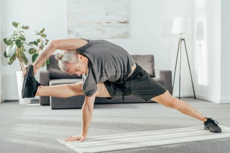 athletic adult man in sportswear stretching on yoga mat at home 