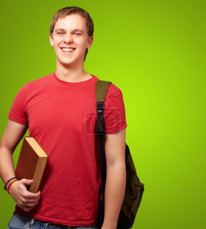 Portrait of young student holding book and carrying backpack ove