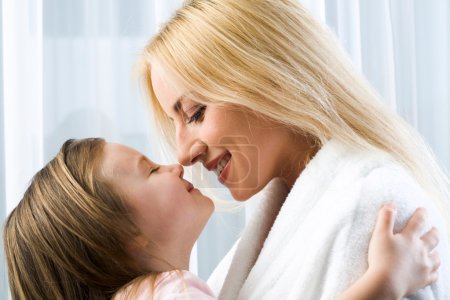 Little blond girl hugging her smiling mother reaching to kiss her